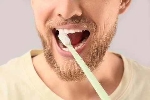 Young bearded man brushing teeth on light background, closeup Stock Photos