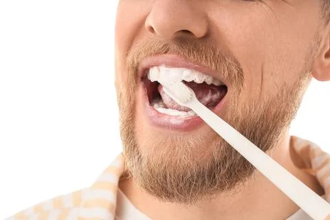 Young bearded man brushing teeth on white background, closeup Stock Photos
