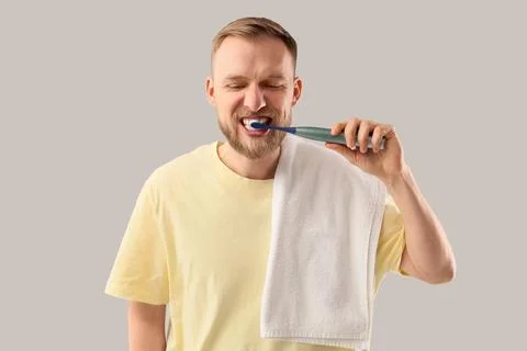 Young bearded man brushing teeth with electric toothbrush on light background Stock Photos