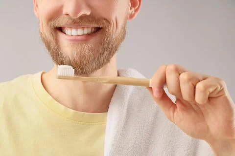 Young bearded man brushing teeth on light background, closeup Stock Photos
