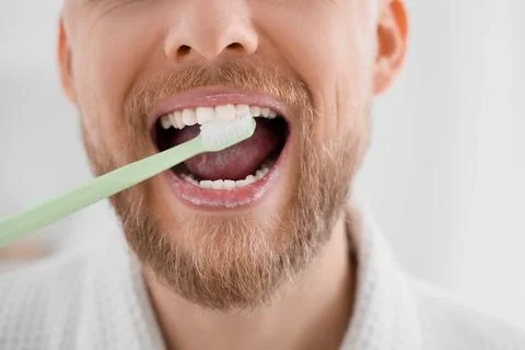 Young bearded man brushing teeth in bathroom, closeup Stock Photos