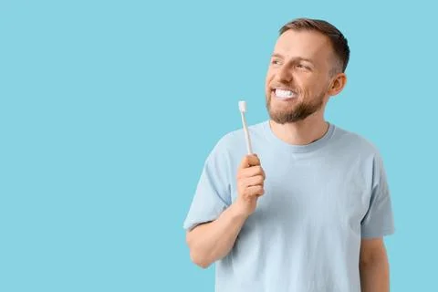 Young bearded man brushing teeth on blue background Stock Photos