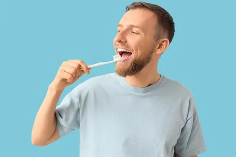 Young bearded man brushing teeth on blue background Stock Photos
