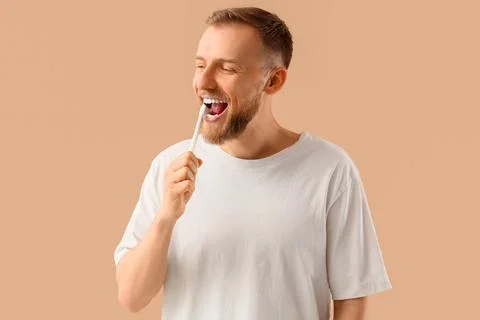 Young bearded man brushing teeth on beige background Stock Photos