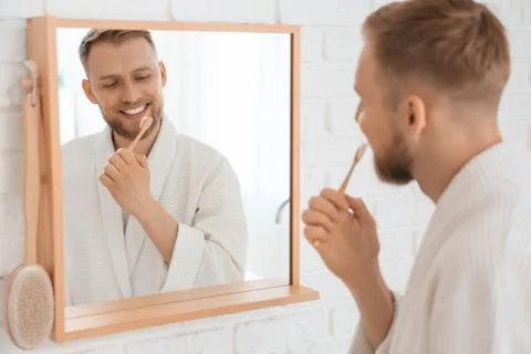 Young bearded man brushing teeth near mirror in bathroom Stock Photos