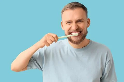 Young bearded man brushing teeth on blue background Stock Photos