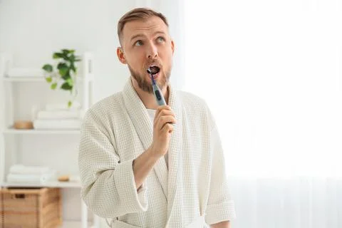 Young bearded man brushing teeth with electric toothbrush in bathroom Stock Photos