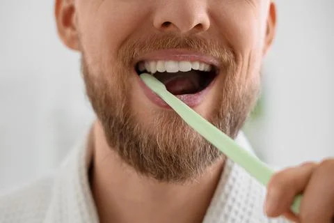 Young bearded man brushing teeth in bathroom, closeup Stock Photos