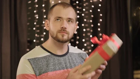 Young bearded man in casual clothes with a gift box at home against the Stock Footage 128923213