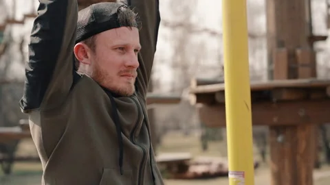 Young bearded man is doing exercise on horizontal bar on spring day in park. Stock Footage 133213998