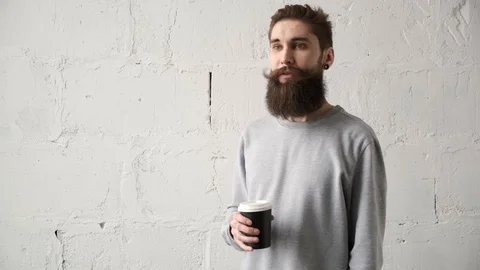 Young bearded man drink coffee looking out window. happy programmer during break Stock Footage 124715859