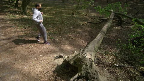 Young Bearded Man in Face Mask Stretching on a Fallen Tree Stock Footage 130850511