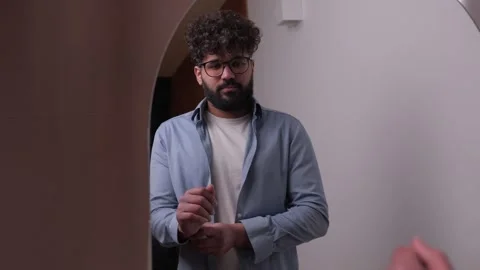 Young bearded man getting ready in front of a mirror Vídeos de archivo 348082366