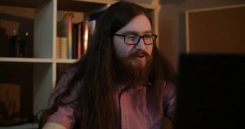 A young bearded man with glasses laughs at the computer Stock Footage 87323591