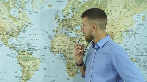 A young bearded man with glasses look at camera on the background of a map Stock Footage 70607715