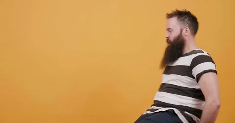 Young bearded man having fun on a rotating chair in front of yellow background Stock Footage 104081280