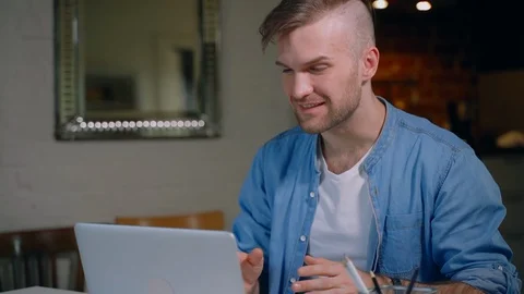 Young bearded man is having video call and using laptop at table in apartment Stock Footage 129519907