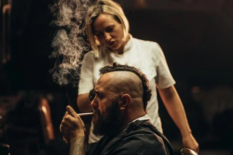 Young bearded man with a mohawk getting haircut by hairdresser and smoking a  Stock Photos