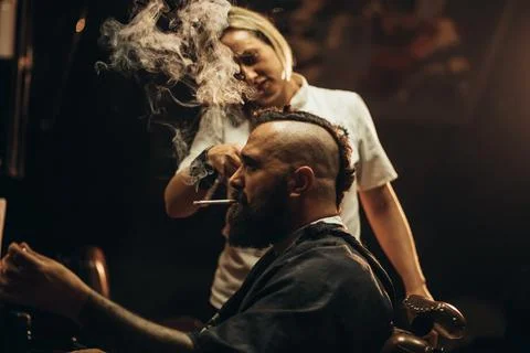 Young bearded man with a mohawk getting haircut by hairdresser and smoking a  Stock Photos