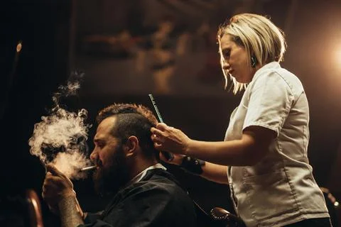 Young bearded man with a mohawk getting haircut by hairdresser and smoking a  Stock Photos
