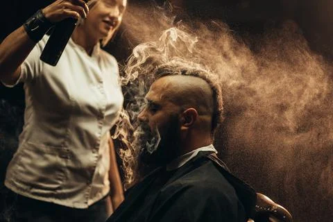 Young bearded man with a mohawk getting haircut by hairdresser and smoking a  Stock Photos