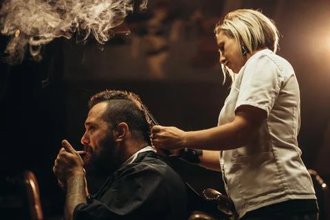 Young bearded man with a mohawk getting haircut by hairdresser and smoking a  Stock Photos