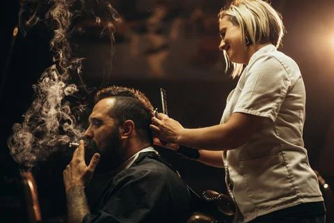 Young bearded man with a mohawk getting haircut by hairdresser and smoking a  Stock Photos
