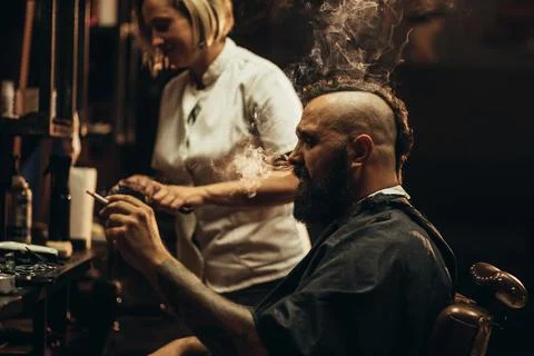 Young bearded man with a mohawk getting haircut by hairdresser and smoking a  Stock Photos