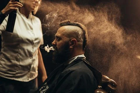 Young bearded man with a mohawk getting haircut by hairdresser and smoking a  Stock Photos