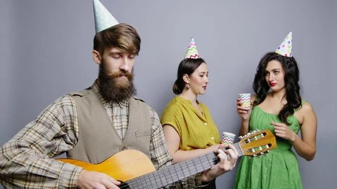 Young bearded man playing guitar for woman in party hat Stock-Footage 81747463