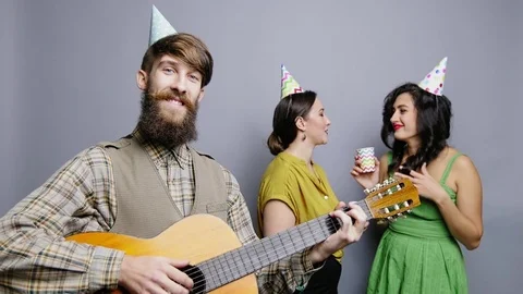 Young bearded man playing guitar for woman in party hat Stock Footage 81747908