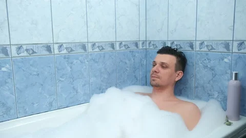Young handsome man in wireless headphones relaxing in bath with foam and  enjoying music Stock Photo
