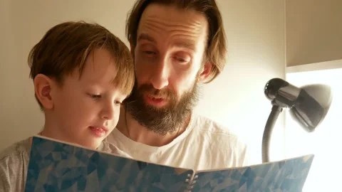 A young bearded man shows a book to his little son telling him something clo Stock Footage 170153563