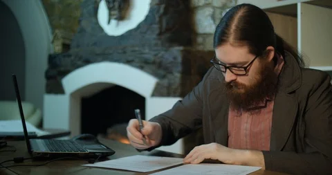 A young bearded man signs papers near the fireplace Stock Footage 87323474