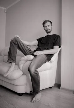 Young bearded man sits and rests on sofa. Stock Photos