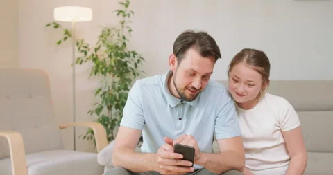 Young bearded man sits on the sofa, holding smartphone, and shows something to Stock Footage 140154201