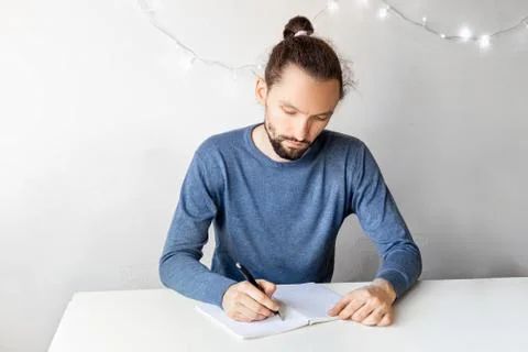 Young bearded man sitting at the table at home writing down goals for the new Stock Photos