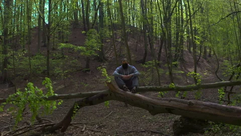 Young Bearded Man Sitting on Tree Branch and Taking Off Face Mask Stock Footage 130762478