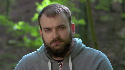 Young Bearded Man Sitting on Tree Branch and Putting on Protective Face Mask Stock Footage 130762550