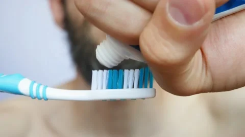 A young bearded man squeezes toothpaste onto a brush and brushes his teeth Stock Footage 133906528