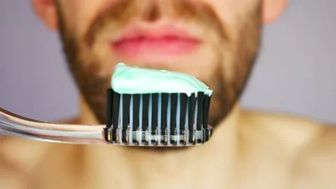 A young bearded man squeezes toothpaste onto a brush and brushes his teeth Stock Footage 144444910