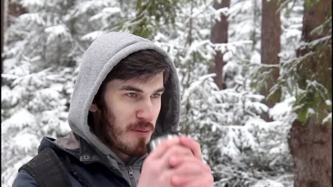 Young bearded man standing in front of a beautiful snowy forest drinking tea Stock Footage 329499213