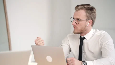 Young bearded man is talking to colleague and working with laptop at table in Video stock 133219782