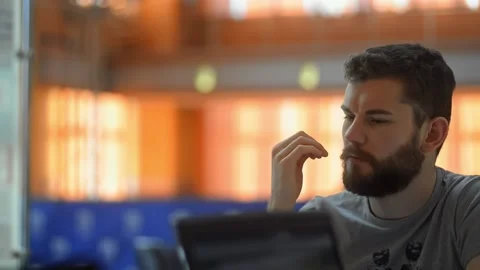 Young bearded man is talking with colleagues, sitting at table in modern office Stock Footage 135812940