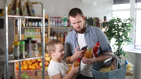 Young bearded man with tween son buying organic bottled juices in grocery shop Stock Footage 341533333