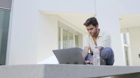 Young bearded man typing on his laptop sitting on a bench Stock Footage 171835182