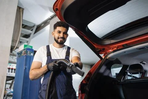 Young bearded man in uniform doing chemical cleaning of car trunk 스톡 사진