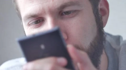 A young bearded man uses his mobile phone. Close-up shot, focus on eyes Stock Footage 68885384