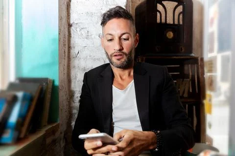 A young bearded man using the cell phone in an urban pub in the city Stock Photos