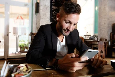 A young bearded man using the cell phone in an urban pub in the city Stock Photos